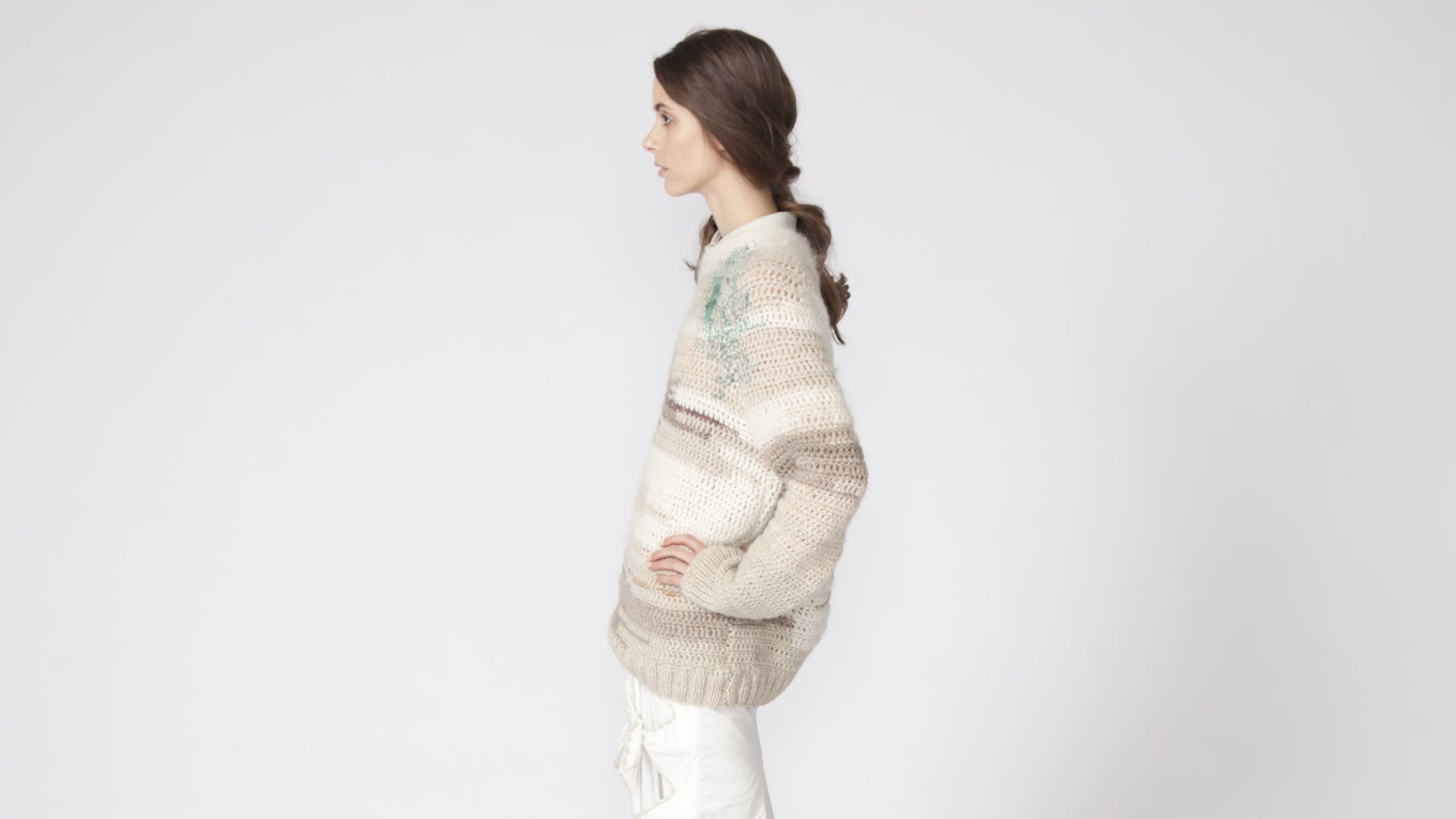 Modella di profilo con un lungo maglione color panna su fondo chiaro da studio