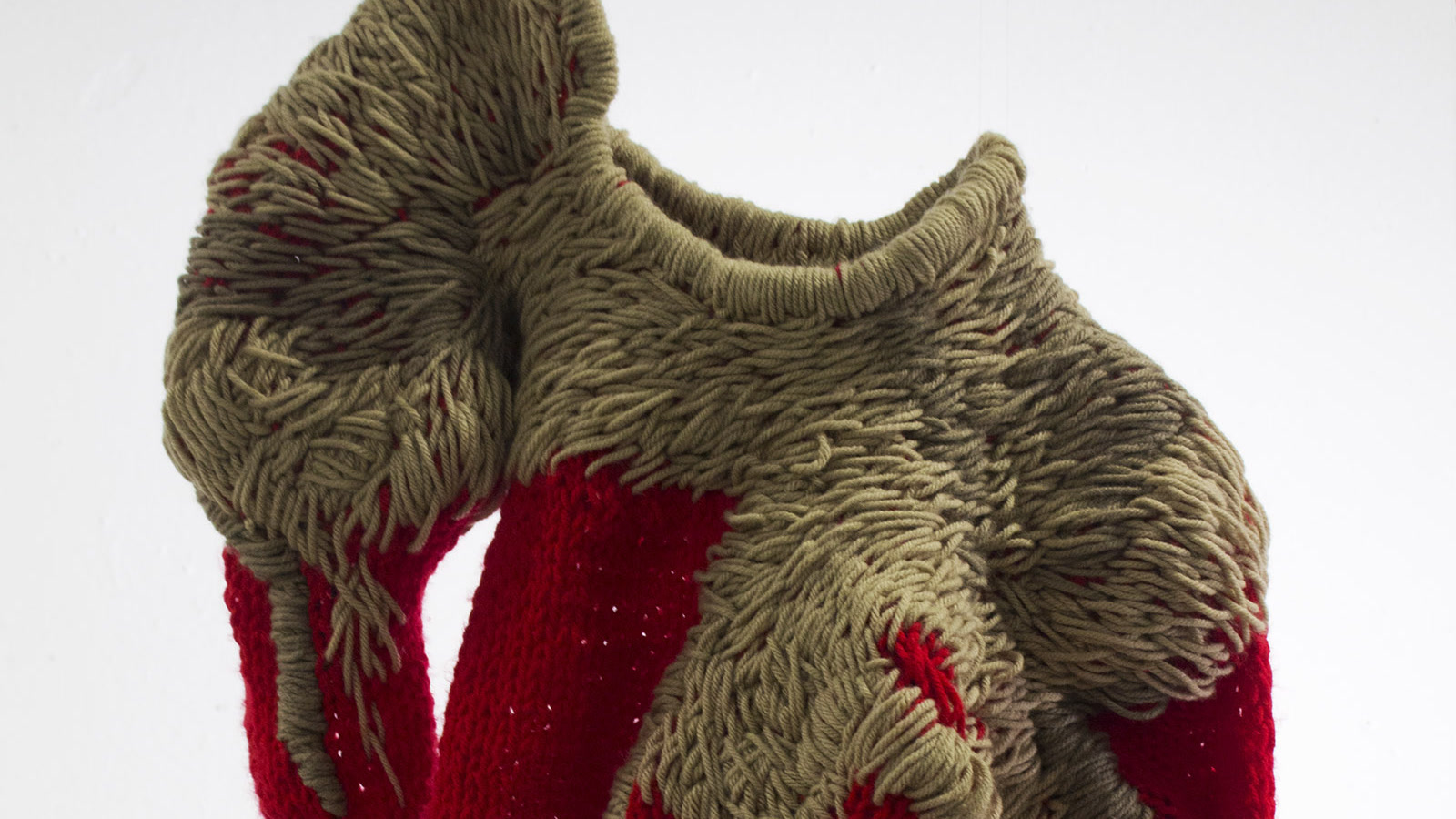Dettaglio ravvicinato di un capo scultoreo rosso e tortora con maglie esposte e bordi fittamente avvolti