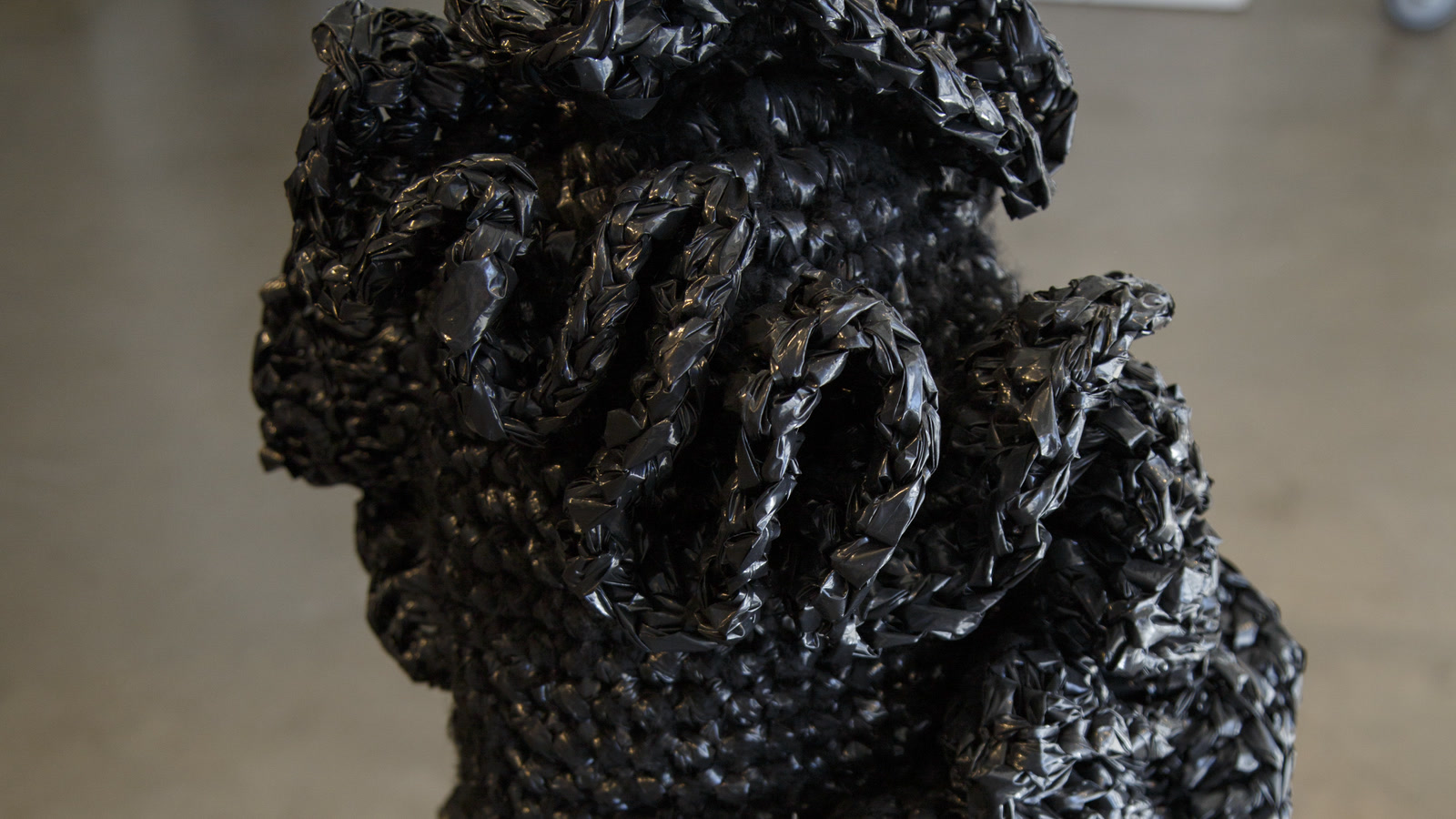 Close view of a black knitted sculptural construction made from broad reflective tape-like material