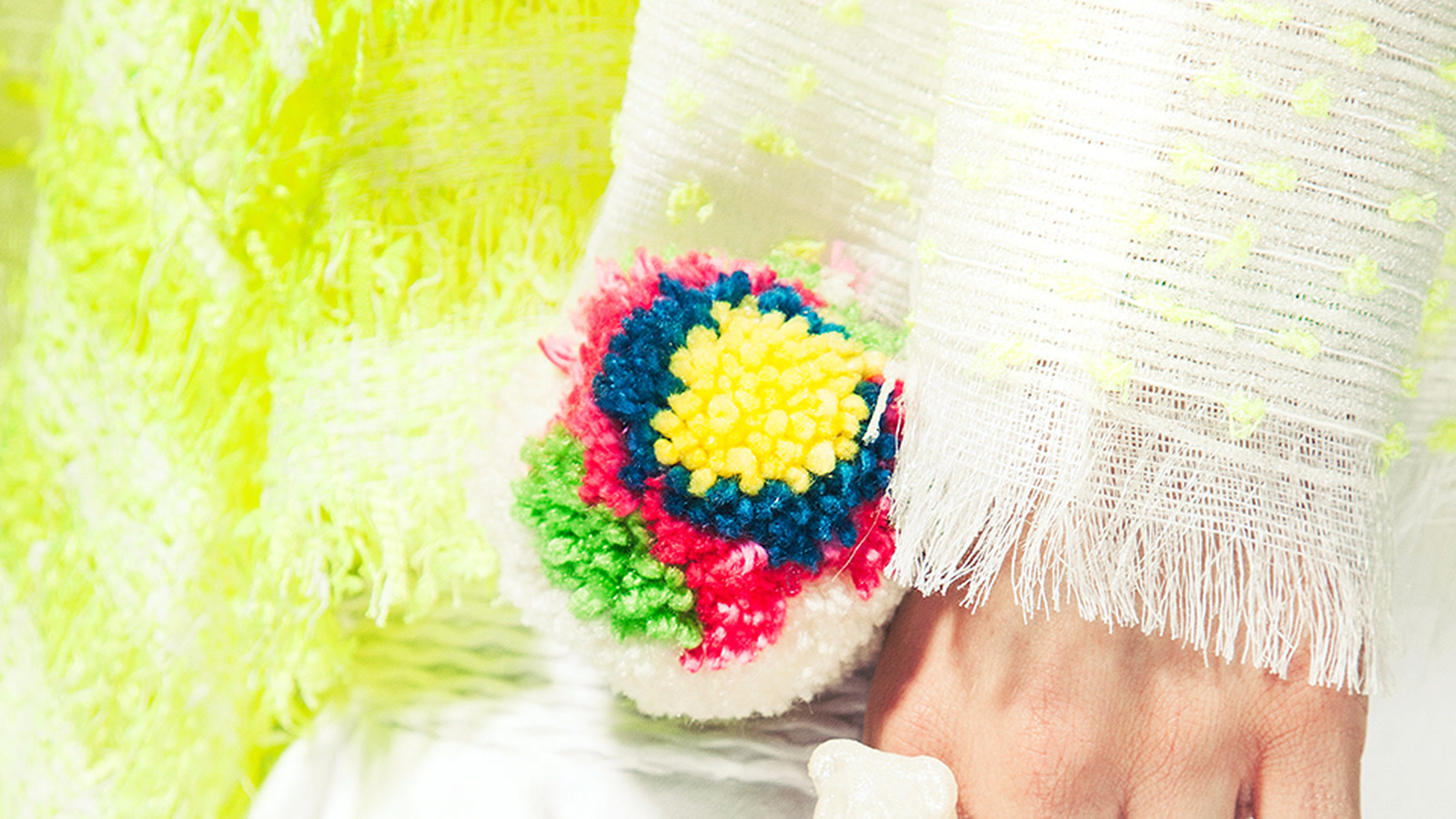 Close view of fluorescent yellow and white knitted textiles with a multicoloured yarn detail under bright studio light
