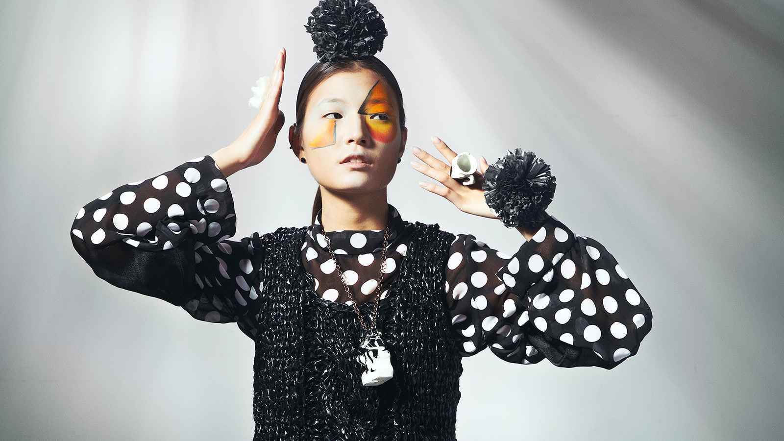 Editorial model in a black knitted vest and spotted sleeves with orange and yellow face colour