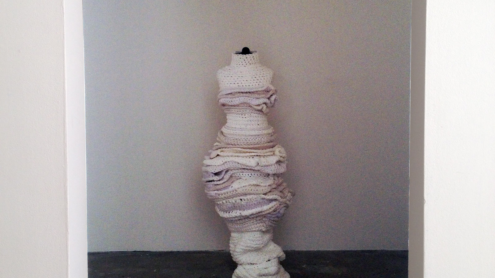 White knitted forms stacked around a mannequin in a grey gallery alcove