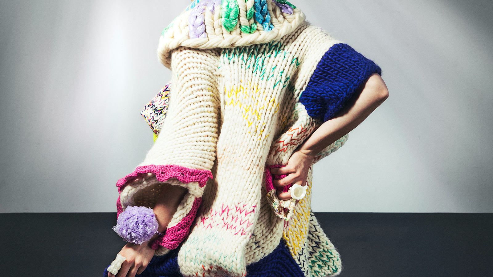 Back view of a sculptural cream knitted garment assembled from contrasting structures and coloured joining yarns