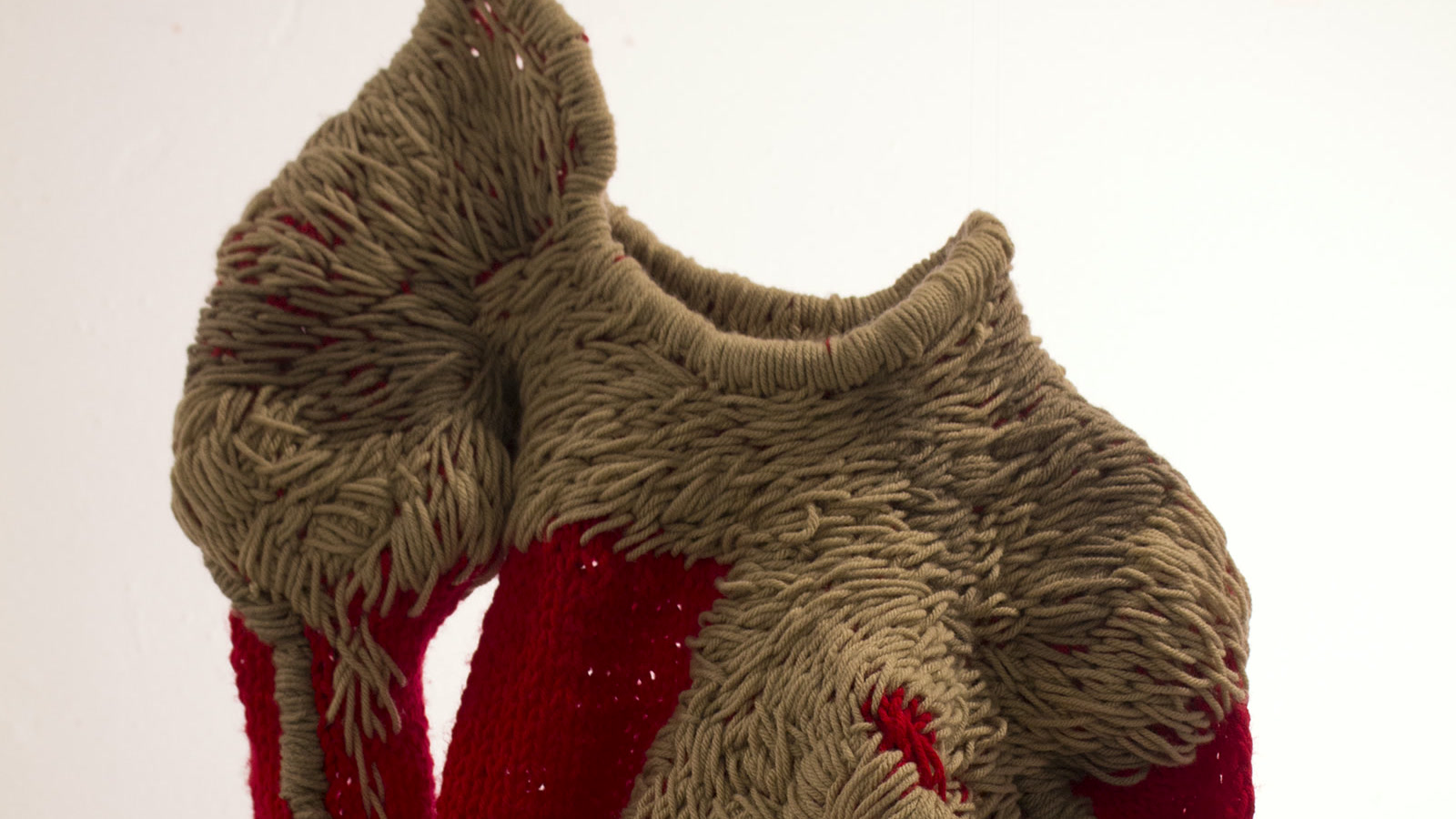 Sculptural red and taupe knitted garment with long exposed yarn loops and raised surface structure