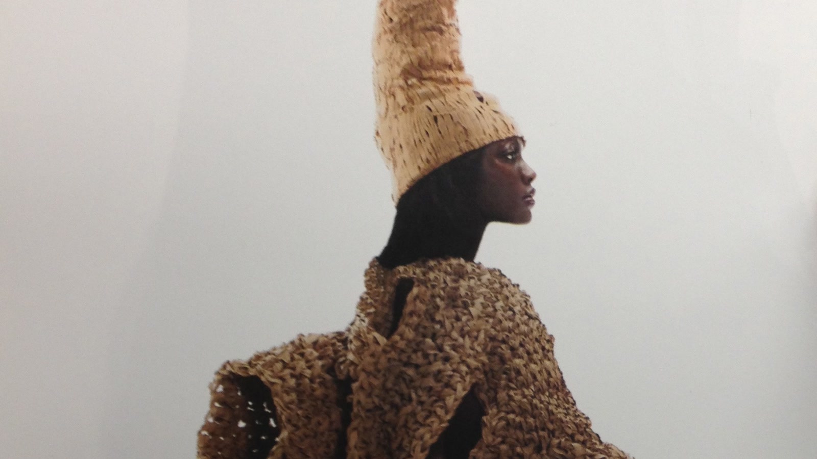 Model in profile wearing a monumental hand-built brown knitted structure and tall sculptural headpiece