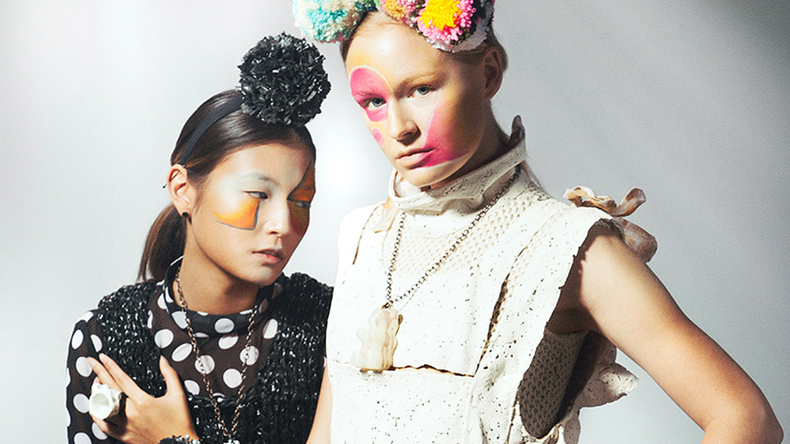 Two editorial models wearing black and chalk garments with different knitted, spotted, matte, and lustrous surfaces under controlled studio light