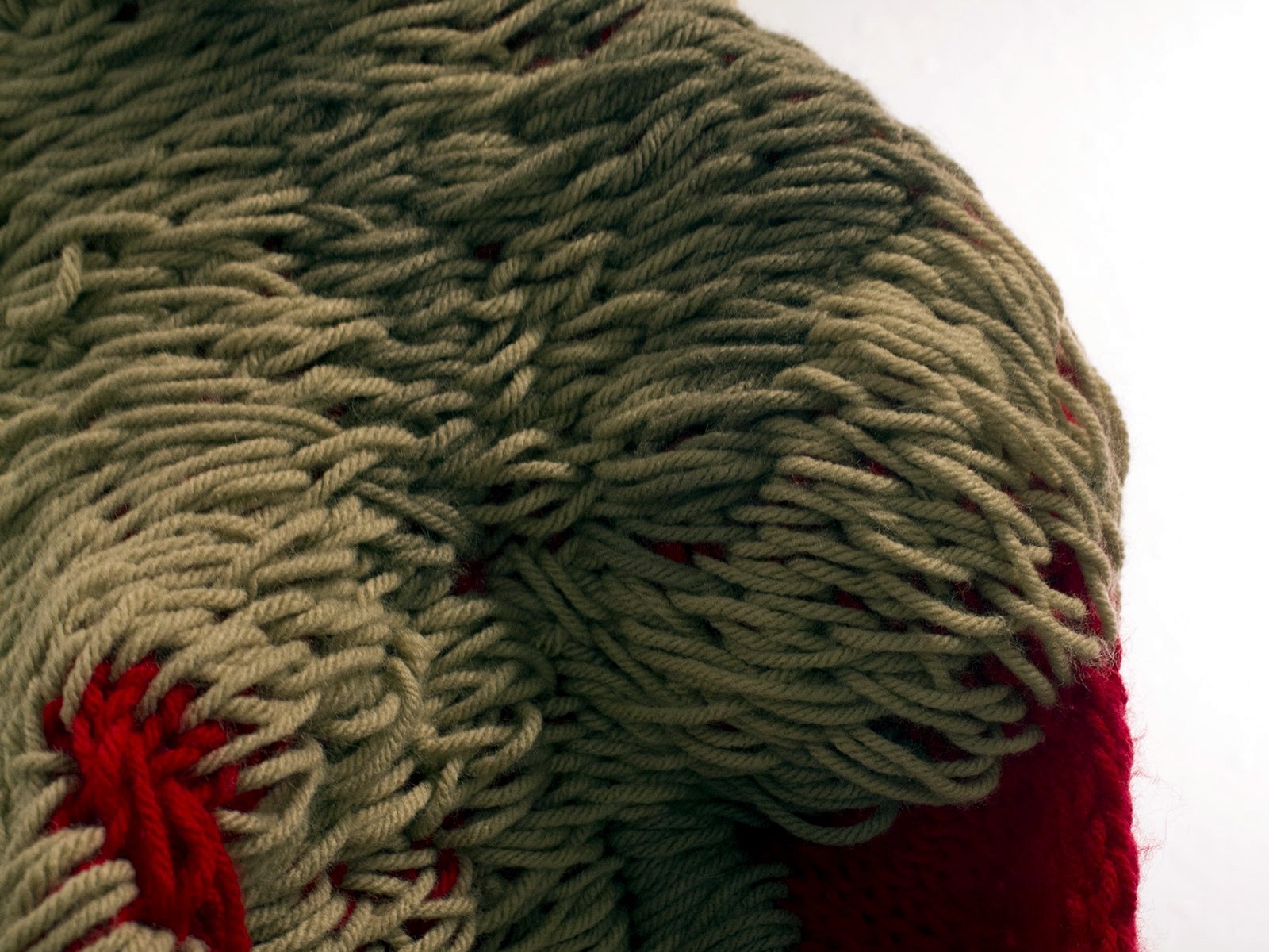 Dettaglio ravvicinato di grandi asole color tortora su una struttura rossa a maglia
