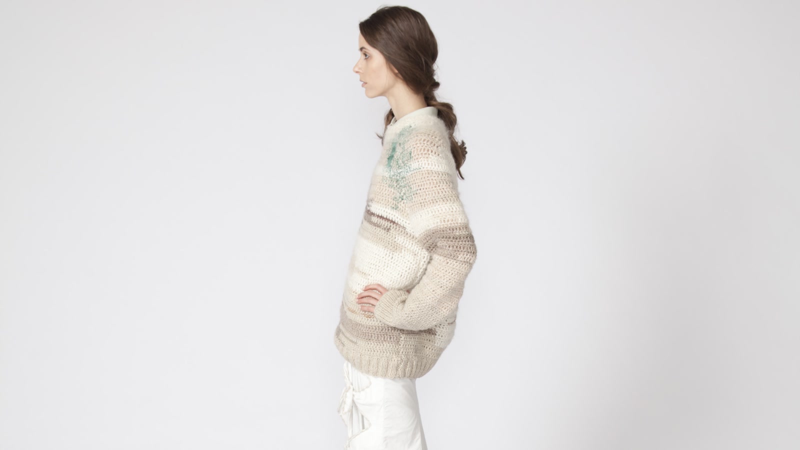 Side view of a model in a pale striped knitted sweater showing garment balance and course direction