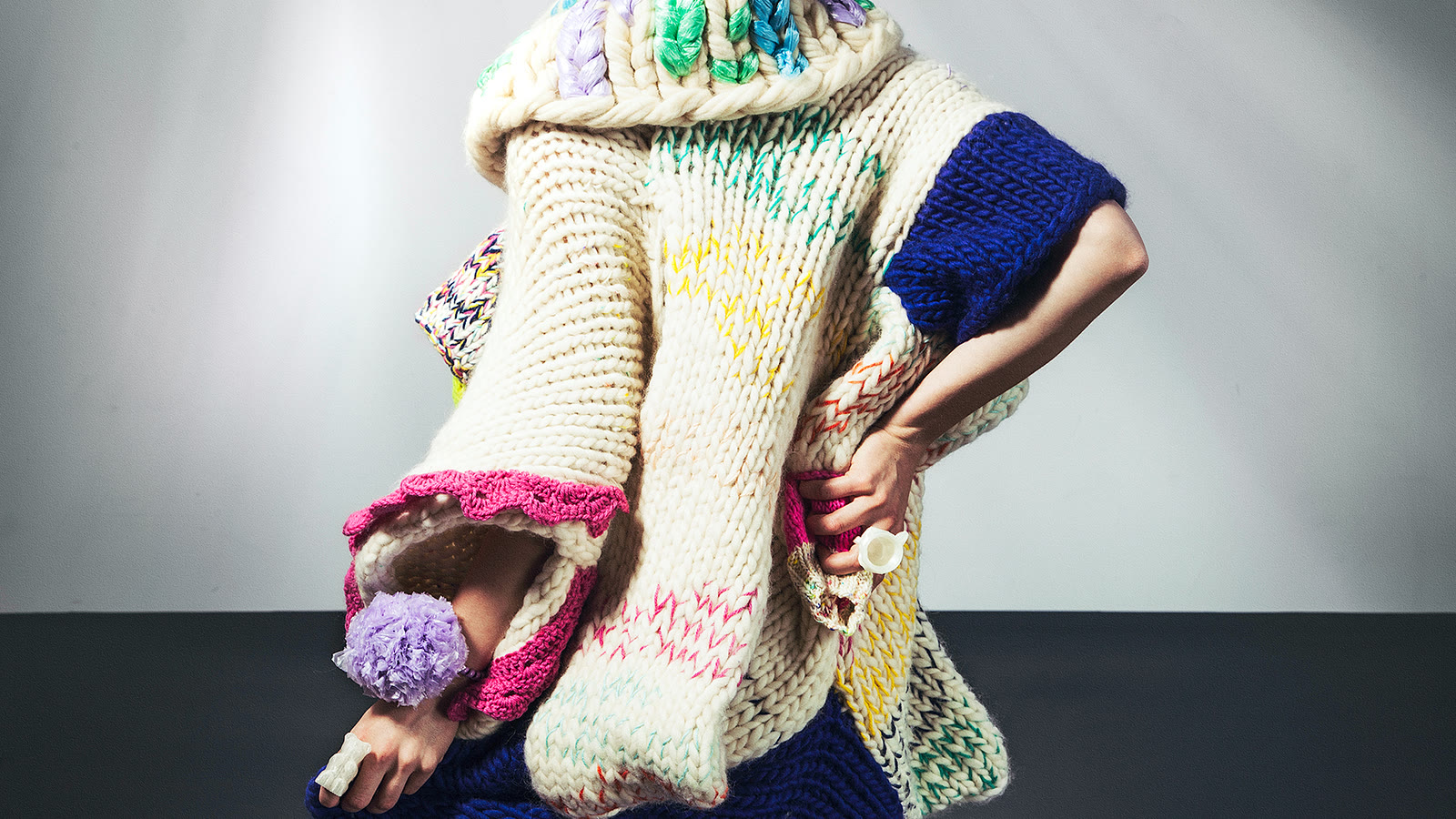 Close view of cream knitted columns with coloured yarn accents across a sculptural garment