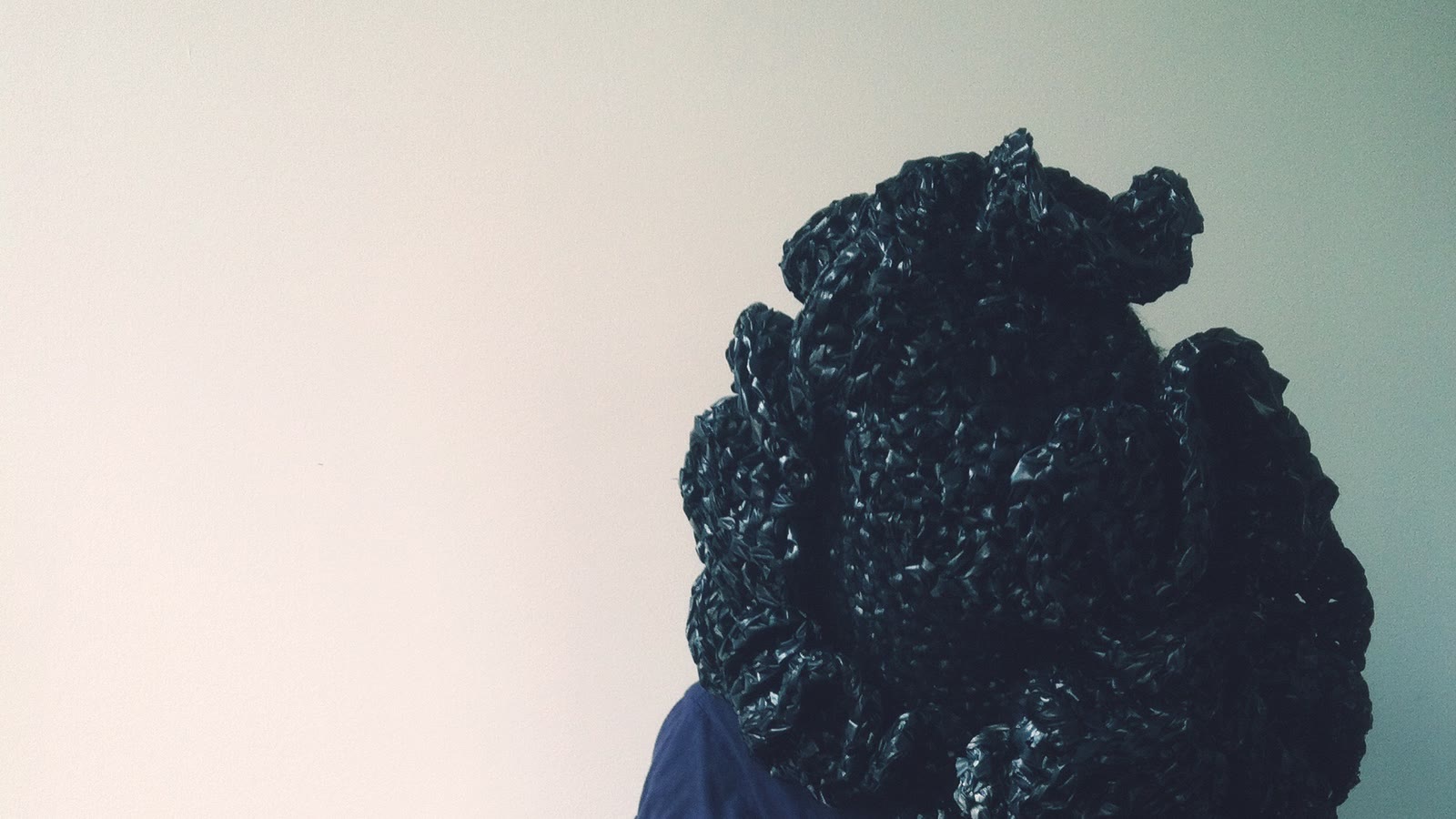 Black sculptural knitted volume projecting from a figure against a pale wall