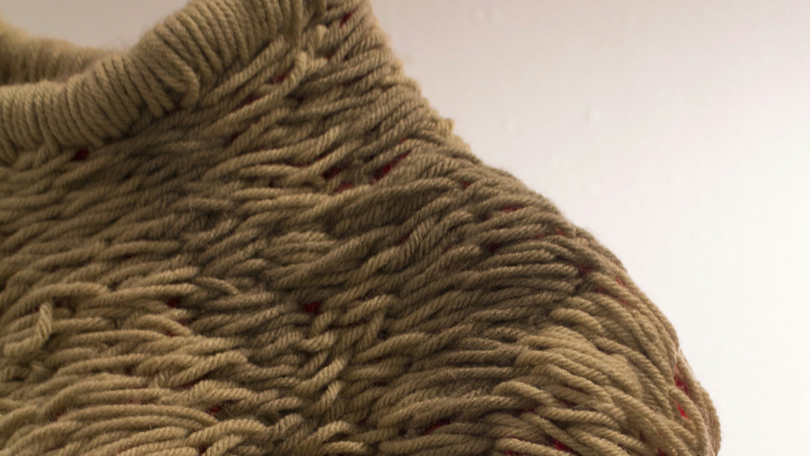 Macro di grandi anse in filato tortora disposte sopra una base rossa a maglia