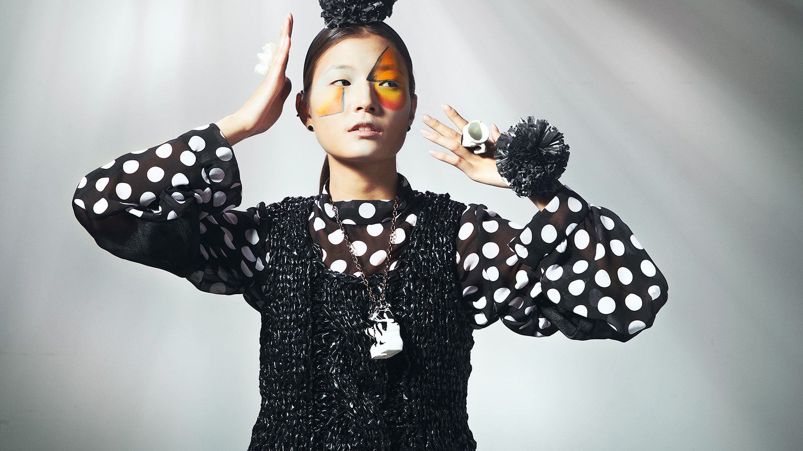 Model wearing an open black knitted structure over a fine translucent textile, showing contrasting material scales