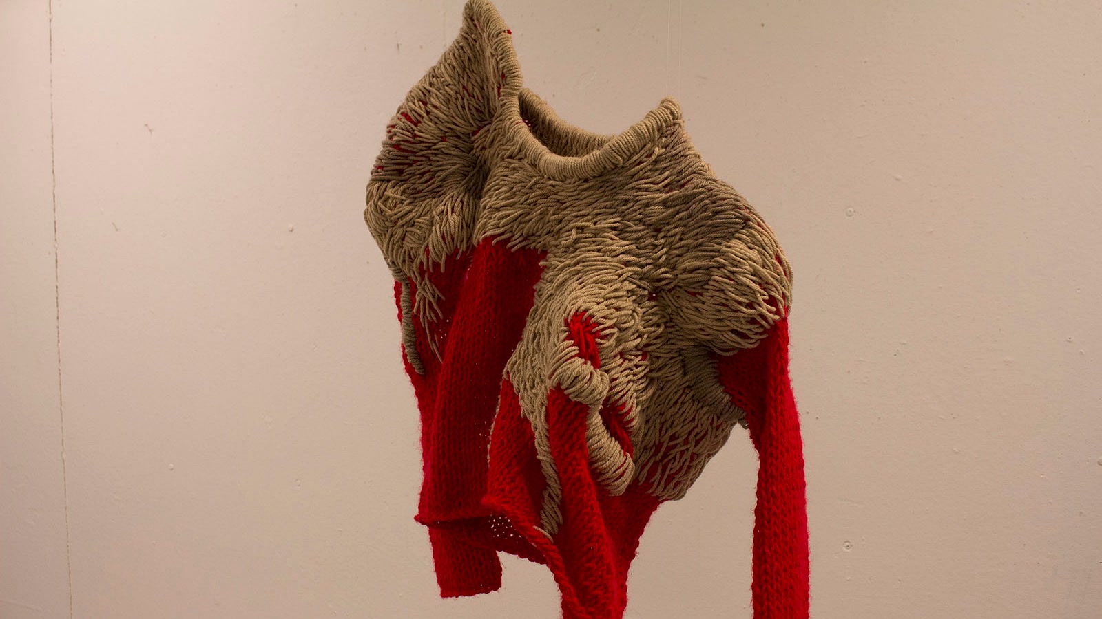Sculptural red and taupe knitted piece with exposed loops, dense wrapped yarn, and intentionally irregular surface structure
