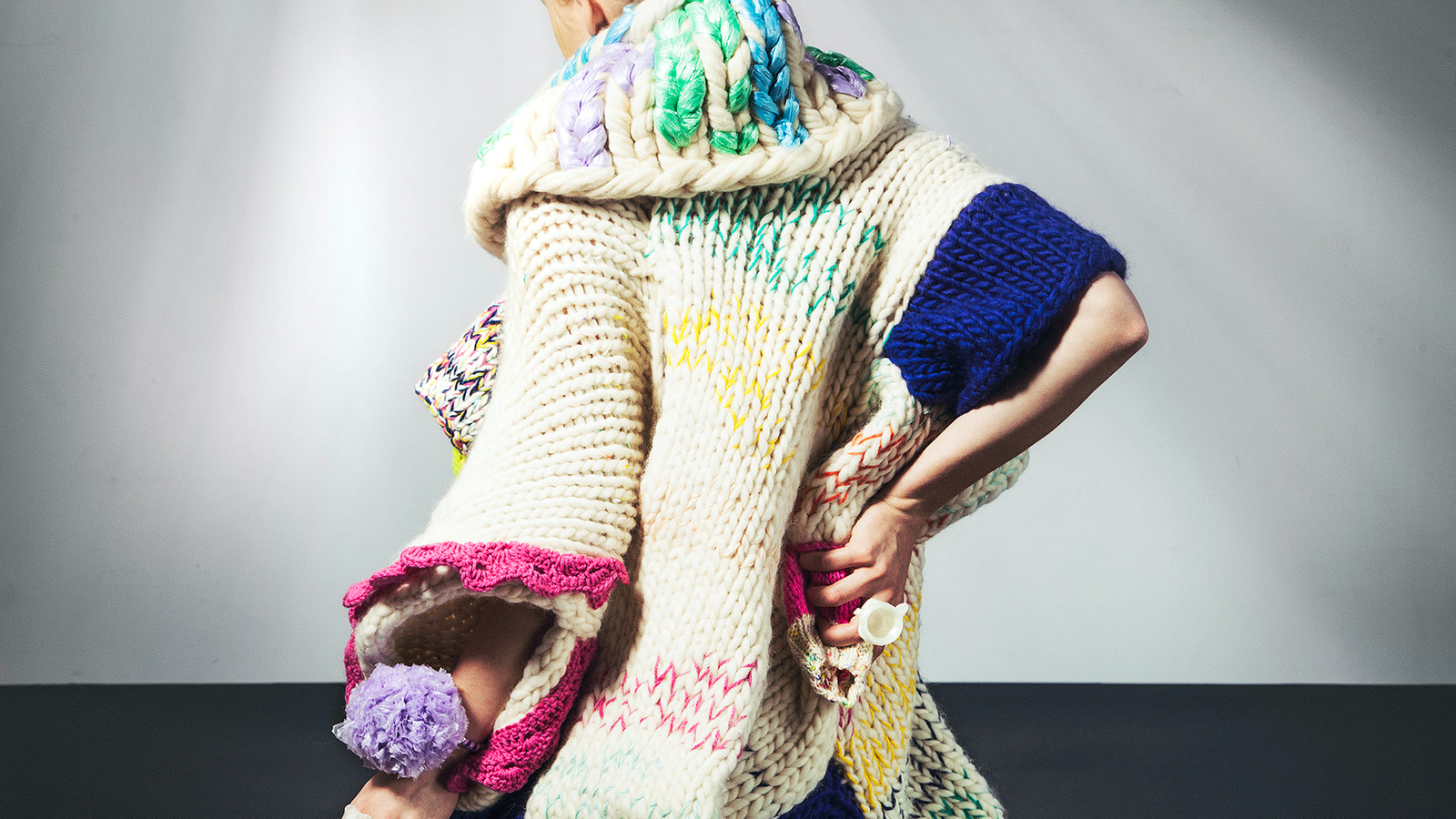 Back view of a model in a sculptural cream chunky knit with blue, green, pink, and lilac yarn details