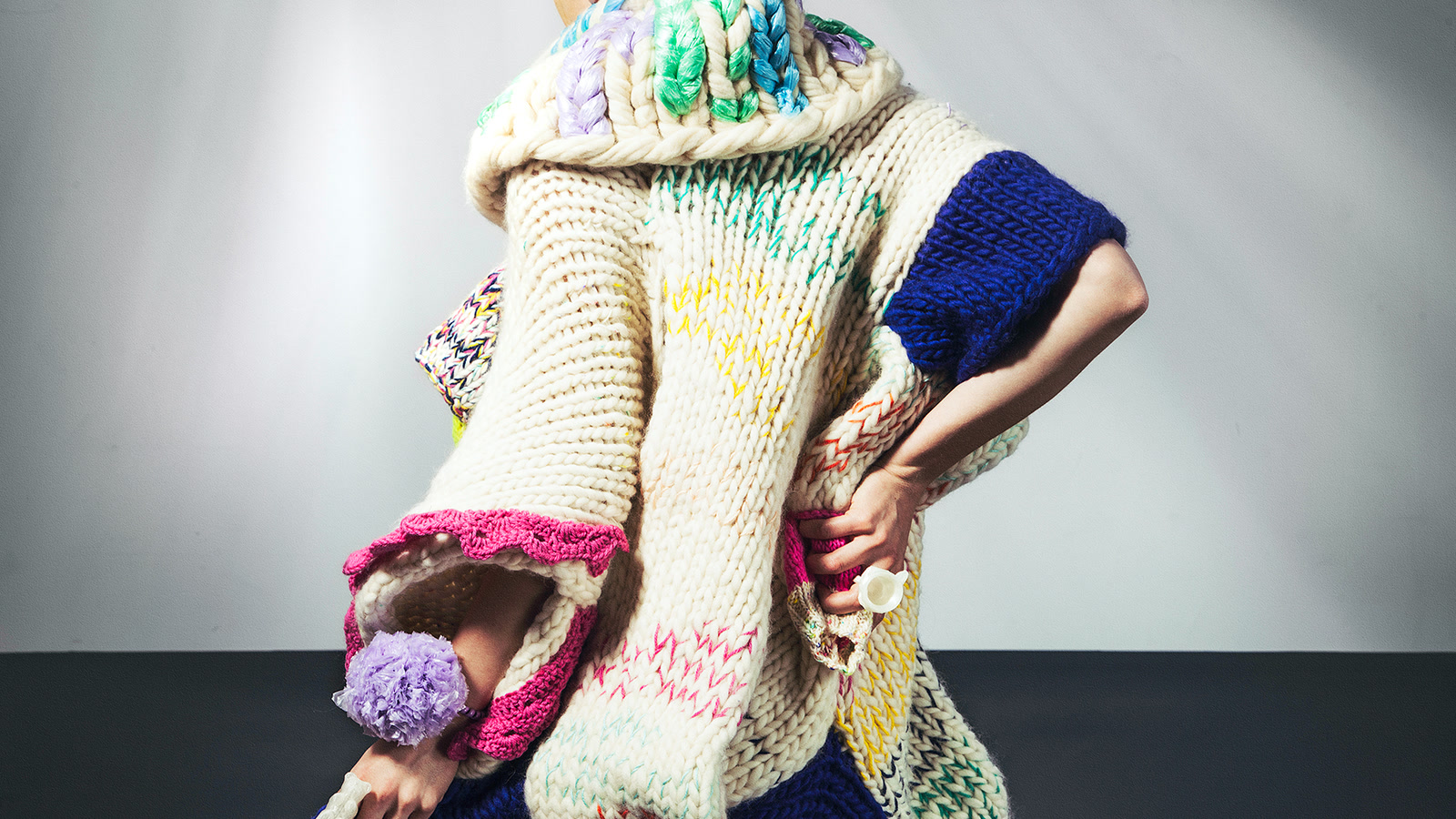 Close view of a sculptural cream knit with large stitches and coloured yarn accents